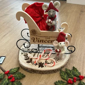 Traîneau de Noël en bois personnalisé avec prénom, accompagné d’un pochon rouge, de deux figurines souris Gry & Sif en feutre, de sucres d’orge et présenté sur un rondin de bois décoratif.